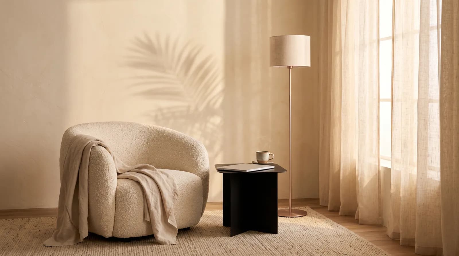 Cream boucle armchair, black side table with a laptop and mug, and a rose-gold floor lamp by sheer linen curtains.